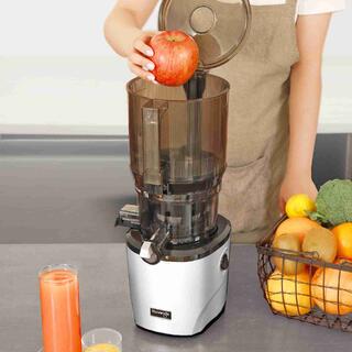 Foto einer Person in der Küche mit einem Korb voller Obst und Gemüse, die einen ganzen Apfel in den Kuvings AUTO10 Slow Juicer legt.